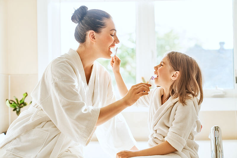 Young mother and daughter brushing their teeth