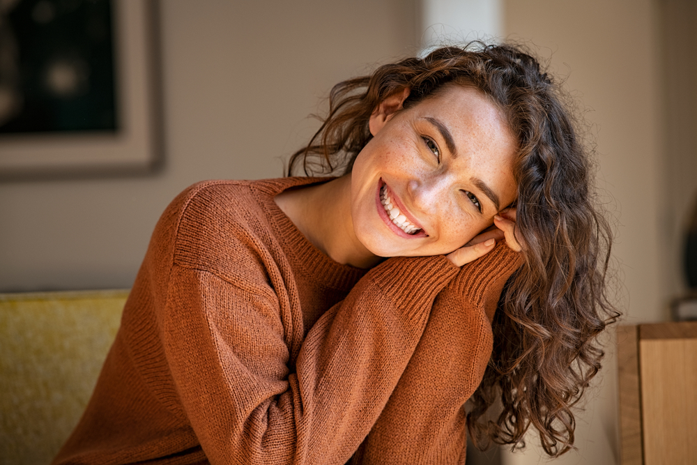Smiling woman with curly hair resting her head on her folded arms