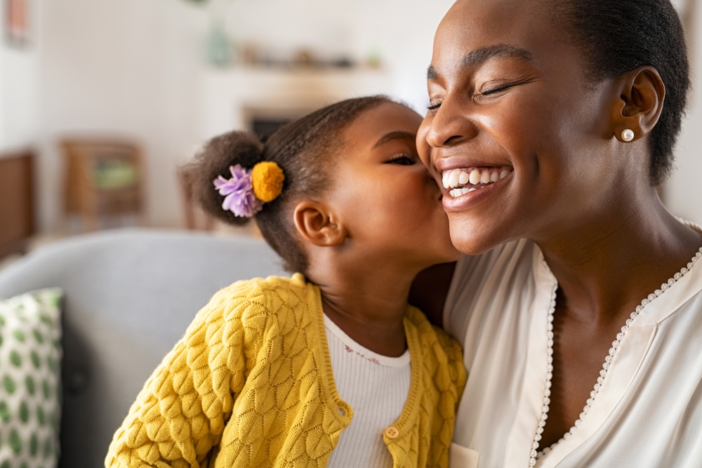 Young girl kissing her smiling mother on the cheek