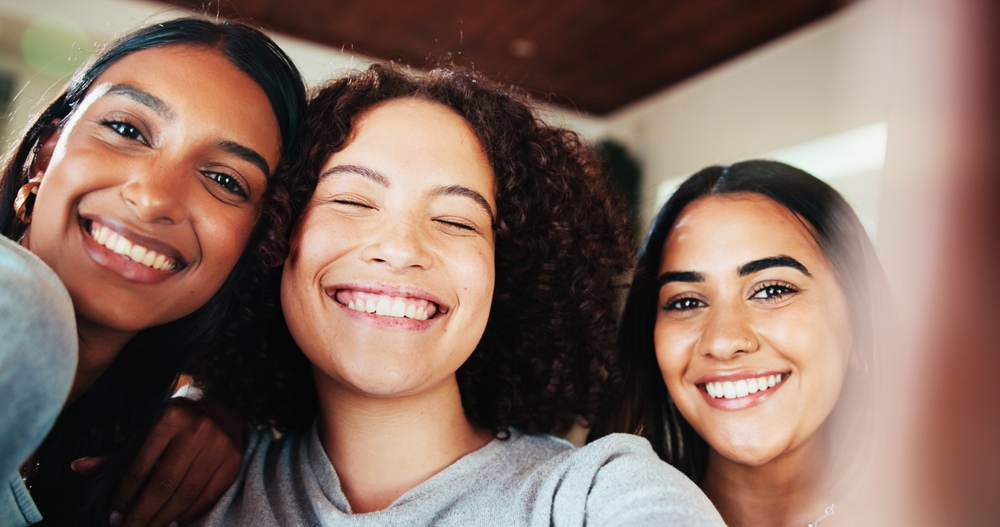 Three smiling young women posing together for a selfie