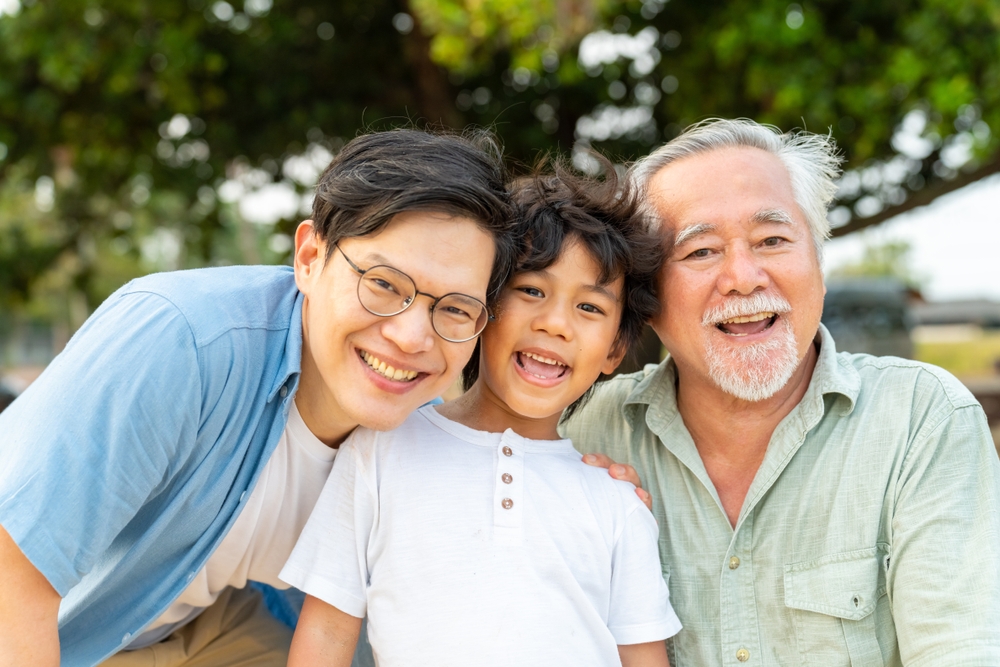 Grandfather, father and young son smiling together outdoors
