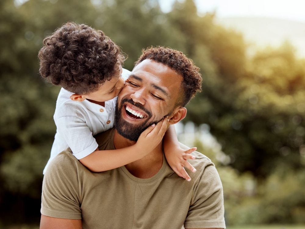 Young boy kissing his smiling father on the cheek outdoors