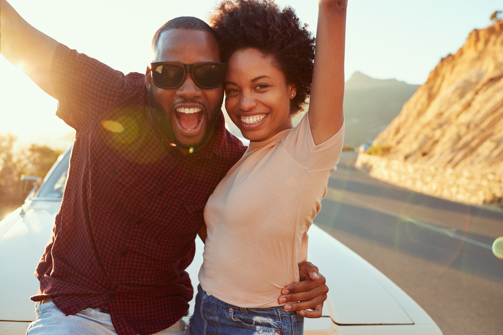 Laughing couple in sunglasses celebrating outdoors at sunset
