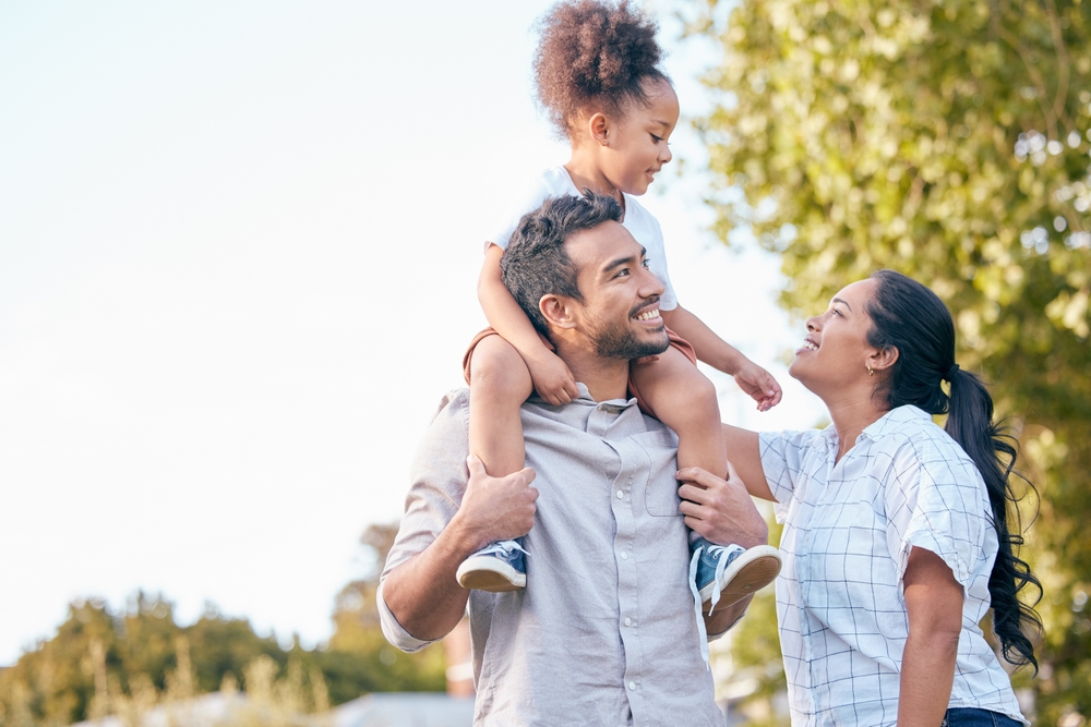 Father carrying his smiling daughter on his shoulders beside her mother outdoors