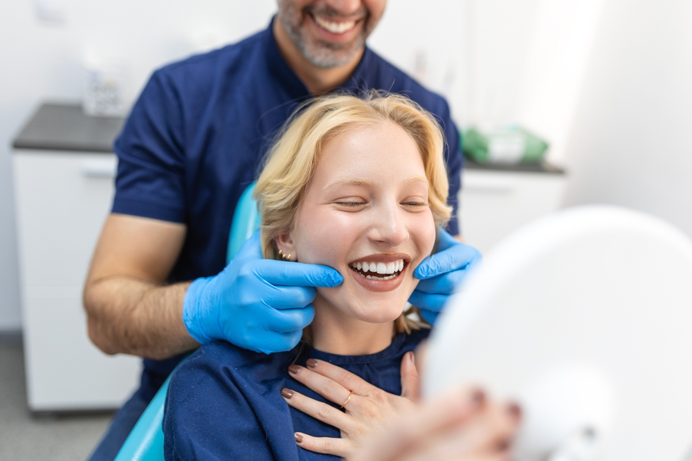 Dentist checking a smiling young woman’s teeth in the dental chair