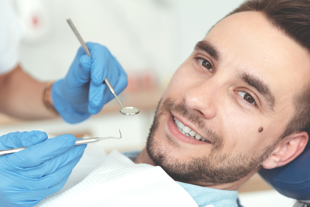 Smiling man in the dental chair while a dentist holds a mirror and probe