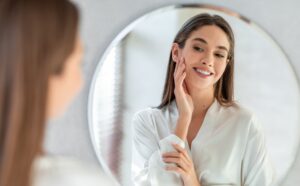 Smiling woman touching her cheek as she looks into a round mirror