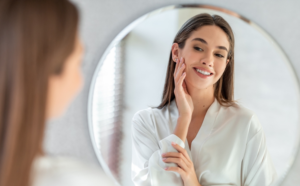Smiling woman touching her cheek as she looks into a round mirror